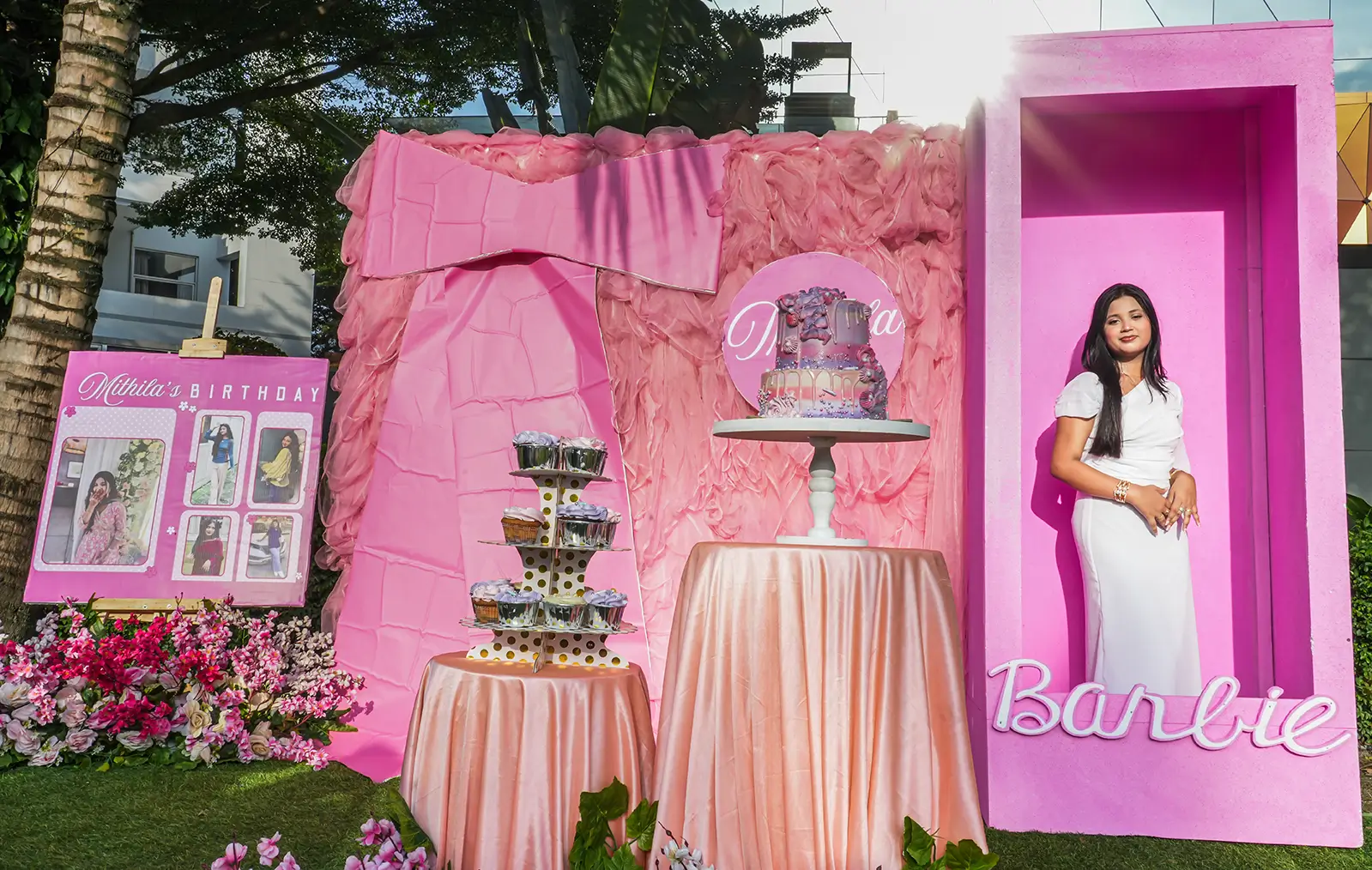 Birthday girl posing inside a life-sized pink Barbie box photo booth next to a dessert table and ruffled pink backdrop at Fortis Downtown Resort, decorated by Look N Feel - Event Solutions.