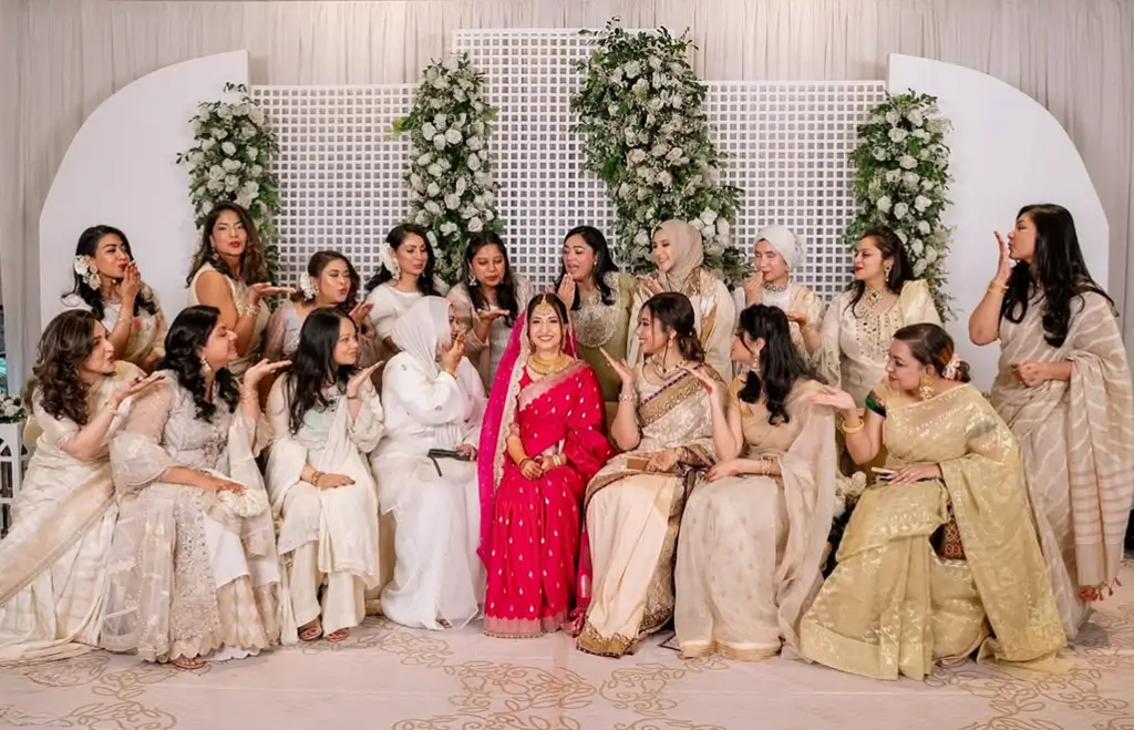 Bride in bright magenta saree seated with bridesmaids in white and ivory outfits on stage at Aloki, decorated by Look N Feel - Event Solutions.
