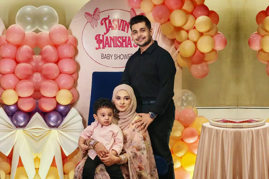 Expecting parents with their toddler posing in front of a peach and pink balloon arch backdrop at a baby shower event in Dhanmondi, decorated by Look N Feel - Event Solutions.